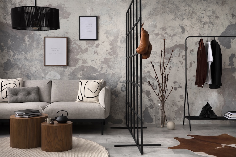 industrialny salon z betonową ścianą i wieszakiem na ubrania salon z cementem na ścianie i kanapą z poduszkami